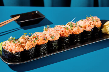 Detailed close-up of gunkan sushi set with crab, shrimp, salmon, tuna, and eel on a black plate against a vivid blue curtain background