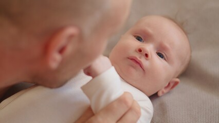 Dad playing with a newborn baby. Cute baby is trying to pronounce sounds while looking at his dad. Face of an active Caucasian baby looking at a parent. Father is playing with his baby.