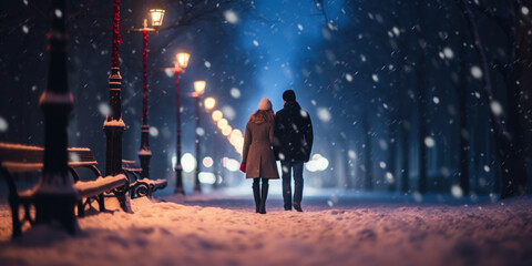 Young couple walking in winter park at night under snowfall. Romantic date concept. - obrazy, fototapety, plakaty