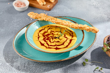 A bowl of pumpkin soup with crostini, served on a gray concrete table. The minimalist composition sets a modern yet comforting tone