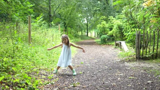 Little beautiful girl in summer dress dancing and playing with leaves in a green park. High quality FullHD footage, Slow motion.