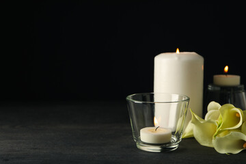 Candles and flowers on wooden table on black background, space for text