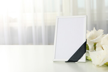 Photo frame with black ribbon and flowers on light background, space for text