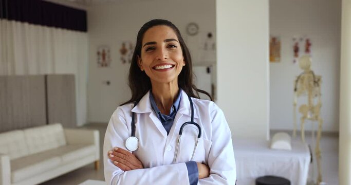 Happy Latina female general practitioner in white coat pose standing at workplace with arms crossed feels confident looks satisfied with career in private clinic. Professional medical worker portrait