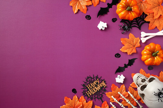 Halloween flat lay composition. Orange maple leaves, pumpkins, skull, ghosts, bats, skeleton hands on purple background. Top view with copy space.