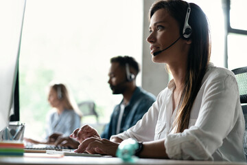 Friendly smiling woman call center operator with headset using computer at office.