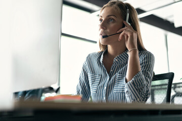 Friendly smiling woman call center operator with headset using computer at office.