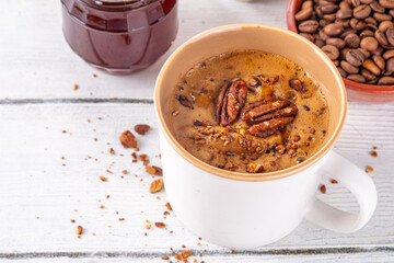 Autumn winter hot spicy drink, Maple Pecan coffee cup on white wooden table with cozy sweater and ingredients copy space
