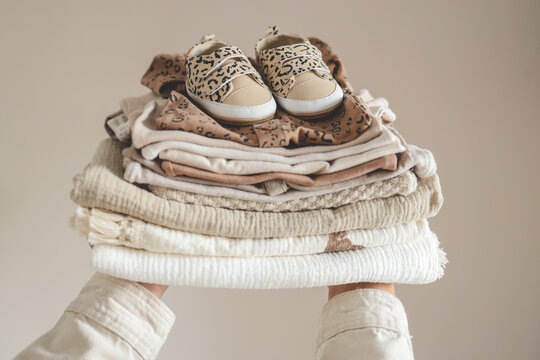 Stack of baby clothes in hand on neutral background