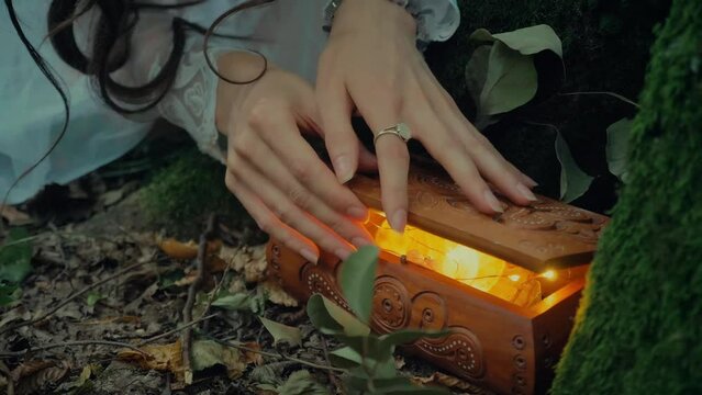 Attractive Dryad Or Forest Fairy found a treasure chest of jewelry and opens it. Charming girl in a transparent white dress in the forest. Mavka Naiad Forest Nymph In A Fairy Tale