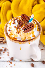 Autumn winter hot spicy drink, Maple Pecan coffee latte with whipped cream cup on white wooden table with cozy sweater and ingredients copy space