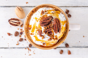 Autumn winter hot spicy drink, Maple Pecan coffee latte with whipped cream cup on white wooden table with cozy sweater and ingredients copy space