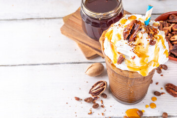 Autumn winter hot spicy drink, Maple Pecan iced coffee latte with whipped cream cup on white wooden table with cozy sweater and ingredients copy space