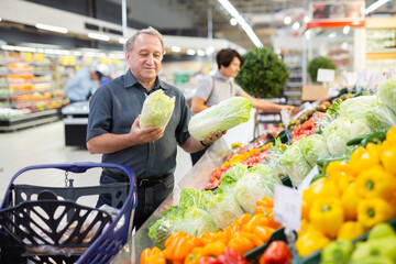 Mature customer selects savoy cabbage with interest in grocery department of supermarket