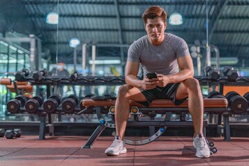 Fototapeta na wymiar Good looking Asian man finds relaxation in the gym, using and checking his phone after a weightlifting exercise training
