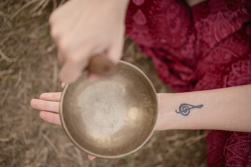 Brazos con tatuaje tocando cuenco tibetano sobre la hierba