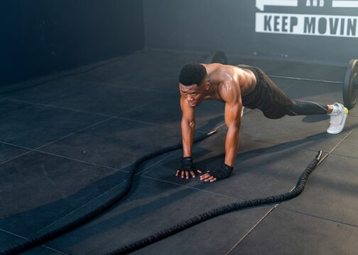 Well-built and muscular, a resilient Black man dominates battle ropes, showcasing exceptional physical power in a high-intensity workout in a training gym