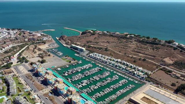 Cinematic aerial point of view of Albufeira marina with luxury urbanisation near the harbour area. Villas in top of the hills, yachts and boats leaving the port.