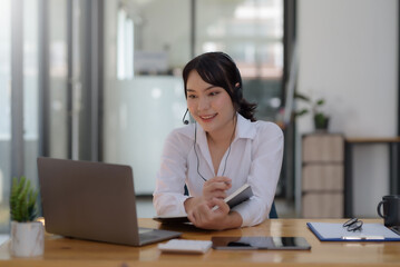 Happy young Asian student woman wearing headphones looking at webcam, looking at camera, during virtual meeting or video call talk.