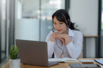 Happy young Asian student woman wearing headphones looking at webcam, looking at camera, during virtual meeting or video call talk.