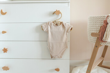 Children's beige bodysuit on a wooden hanger in the nursery