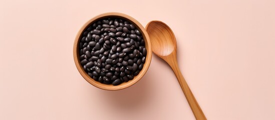 Black bean in wooden bowl and spoon top view isolated pastel background Copy space