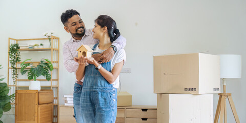 Married Indian couple owners holding house model moving in new home. relocation concept - obrazy, fototapety, plakaty