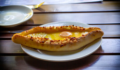 Adjara-style khachapuri, baked dough with egg, cheese and two pieces of butter on a white plate in a cafe.
