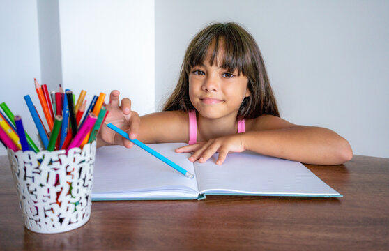 hobby, art and childhood concept - happy smiling girl with pencils and colors drawing picture over home room background