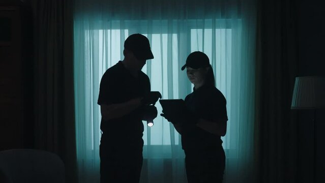 Crime scene creative concept. Police officers with tablet and flashlight standing in the dark living room.