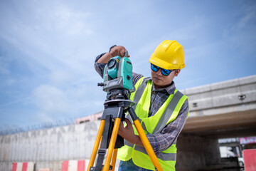 Engineers Surveyor wearing safety uniform ,helmet with equipment theodolite to measurement positioning on the construction site of the road with construct machinery background.