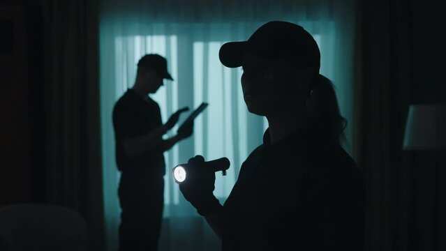Closeup shot of police officers in uniform with tablet and flashlight standing in the dark room. Crime scene creative concept.