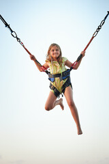 Bungee jumping at trampoline. Little girl bouncing on bungee jumping in amusement park on summer...