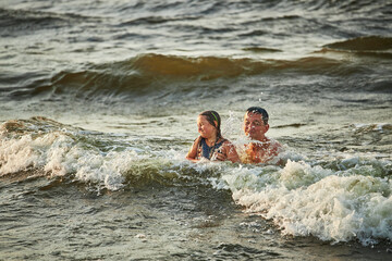 Little girl and her dad playing with waves in the sea. Family summer vacations. Kid playfully splashing with waves. Summer vacation on the beach