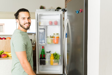 Cheerful young man in the kitchen looking for food in the fridge