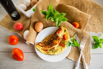 Stuffed omelette with tomatoes on a light wooden background.