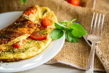Stuffed omelette with tomatoes on a light wooden background.