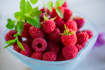Fresh ripe raspberries in a glass bowl on wooden table.