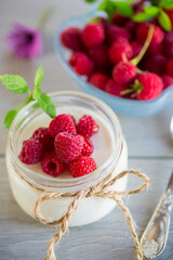 Sweet cooked homemade yogurt with fresh raspberries in a glass jar.