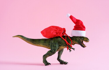Dinosaur in Santa Claus hat holding bag with presents on pink background. Minimal art poster for...