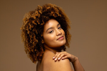 Biracial woman with dark curly hair, smiling and touching shoulder, copy space