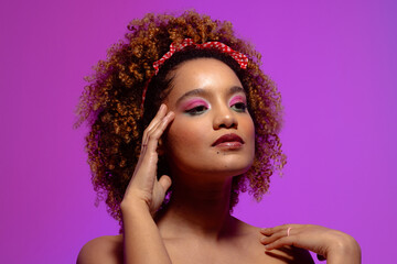 Biracial woman with pink eye shadow and lipstick touching face, purple background