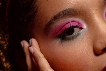 Close up of biracial woman with pink eye shadow and lipstick touching face, purple background