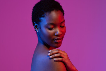 African american woman with short hair, looking down with hand on shoulder, purple background