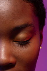 Close up of closed eye of african american woman with short hair on purple background
