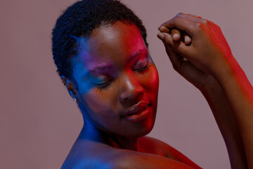 African american woman with short hair and colourful make up touching hands with eyes closed