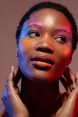 African american woman with short hair and colourful make up, looking away and touching neck