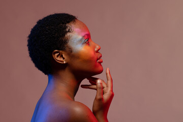 African american woman with short hair and colourful make up, looking up, touching chin, copy space