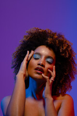 Biracial woman with curly hair and blue eye shadow touching face with eyes closed, copy space