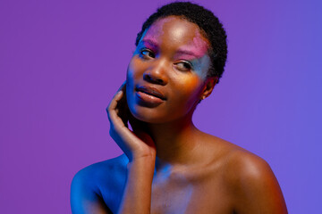African american woman with short hair and colourful make up looking away with hand under chin